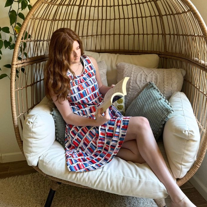 Woman reading in a wicker egg chair, wearing a patterned dress
