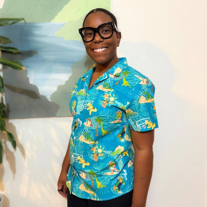 Smiling person with glasses wearing a bright blue and yellow tropical shirt